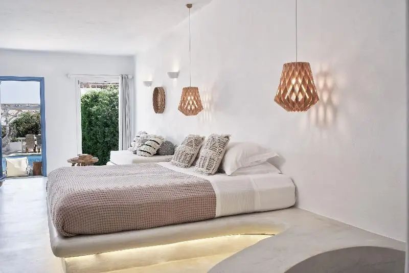 Schlafbereich einer Suite mit hellem Podestbett, Hängeleuchten aus Holz und Blick zum Garten.