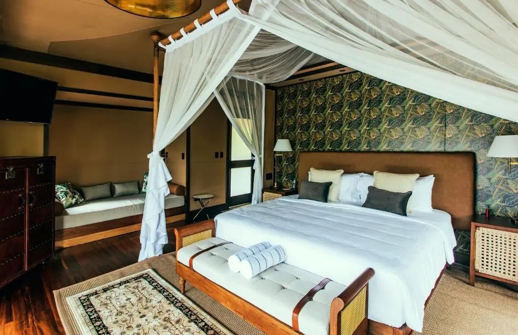 Großes Doppelbett mit Himmelgestell und weißen Vorhängen im Zelt-Bungalow.