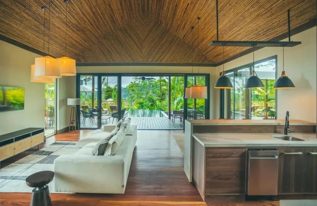 Großzügiger Wohnbereich mit Holzdecke, Sofa und Glasfront mit Blick auf Terrasse und Pool.