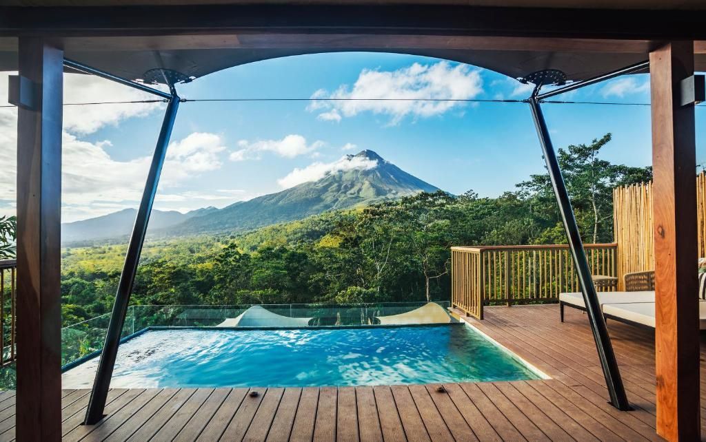 Privater Pool auf einer Holzterrasse mit freiem Blick auf den grünen Regenwald und einen Vulkan.