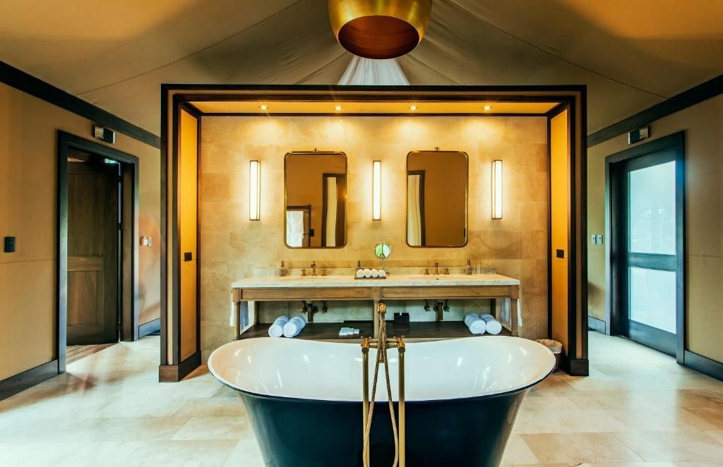 Freistehende dunkle Badewanne vor einem Waschtisch mit zwei Spiegeln und Wandleuchten.