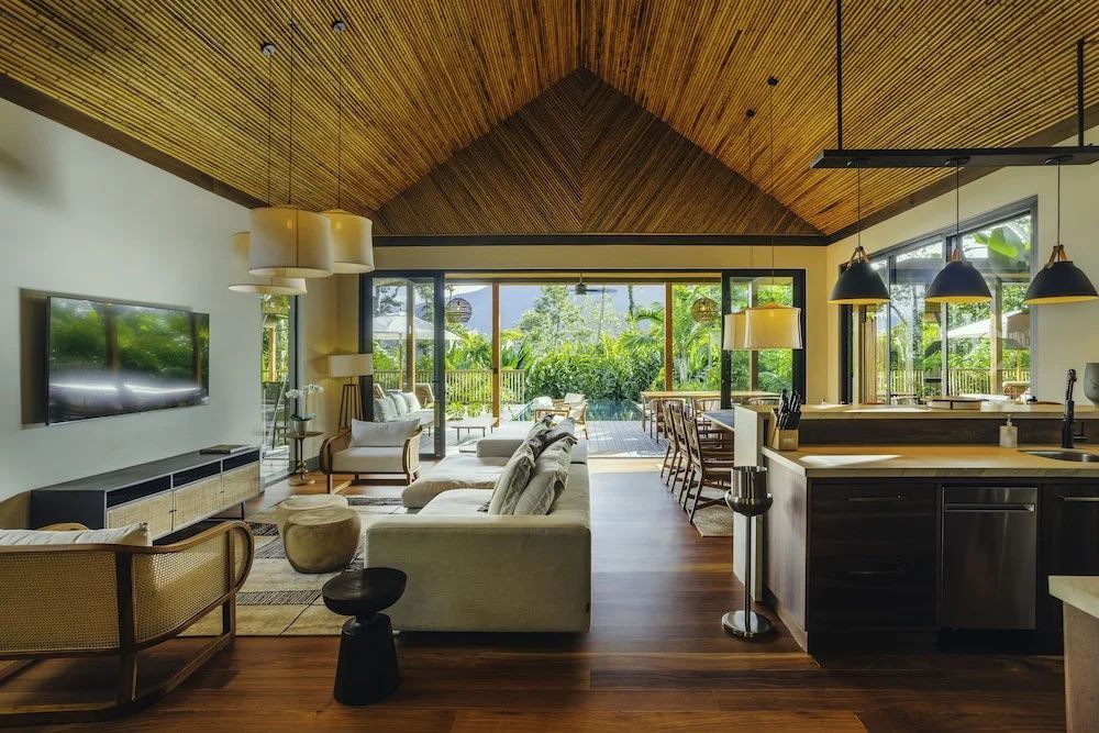 Offener Wohn- und Kochbereich mit hoher Holzdecke, großem Sofa und Blick in die Natur.