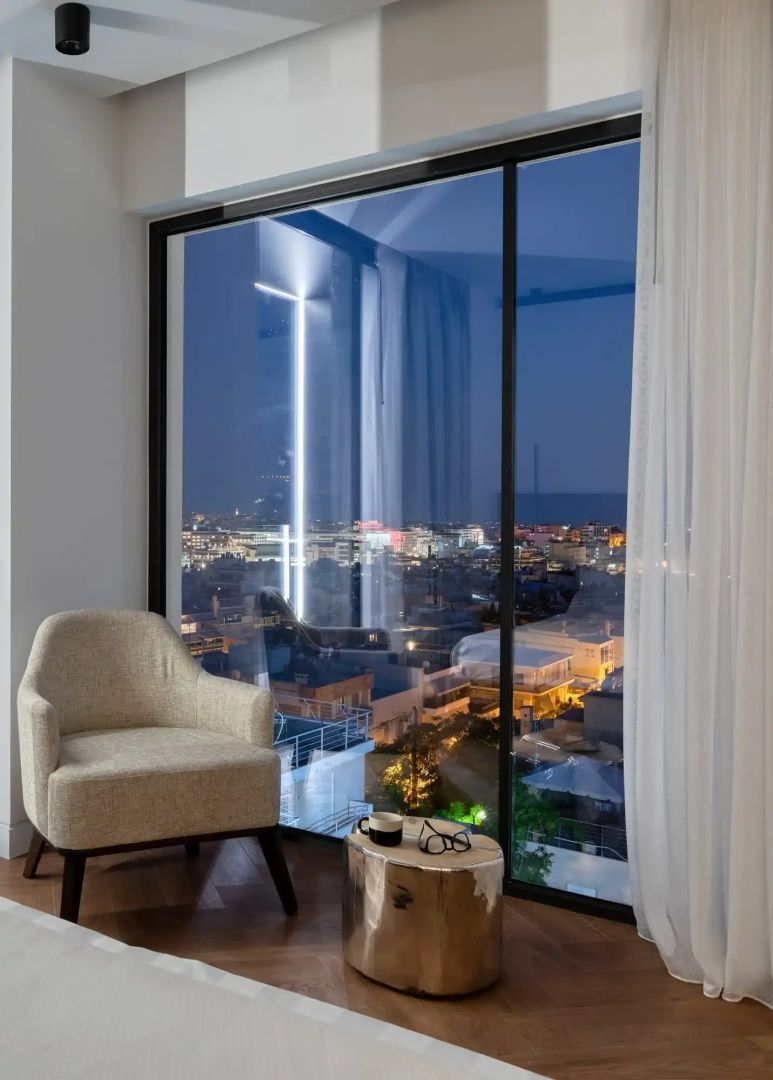Sessel neben einem bodentiefen Fenster mit nächtlicher Aussicht auf die beleuchtete Stadt.
