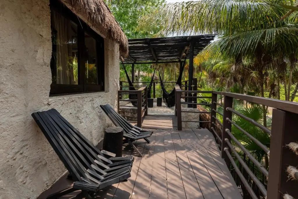 Holzterrasse mit Holzstühlen und Pergola umgeben von tropischen Palmen.