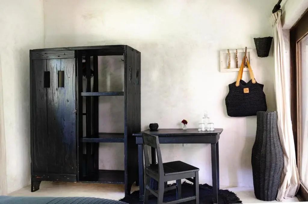 Dunkler Holzkleiderschrank und kleiner Schreibtisch mit Stuhl vor weißer Wand im Hotelzimmer.
