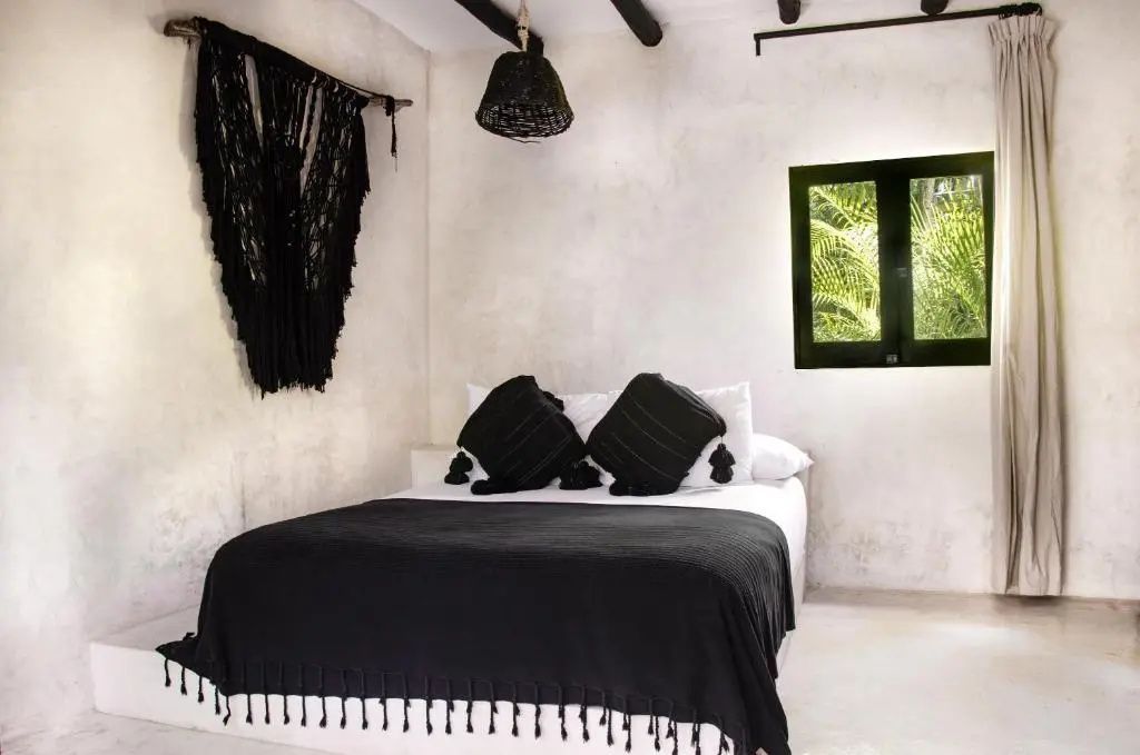 Doppelbett mit schwarzen Kissen und Decke neben einem kleinen Fenster mit Blick ins Grüne.