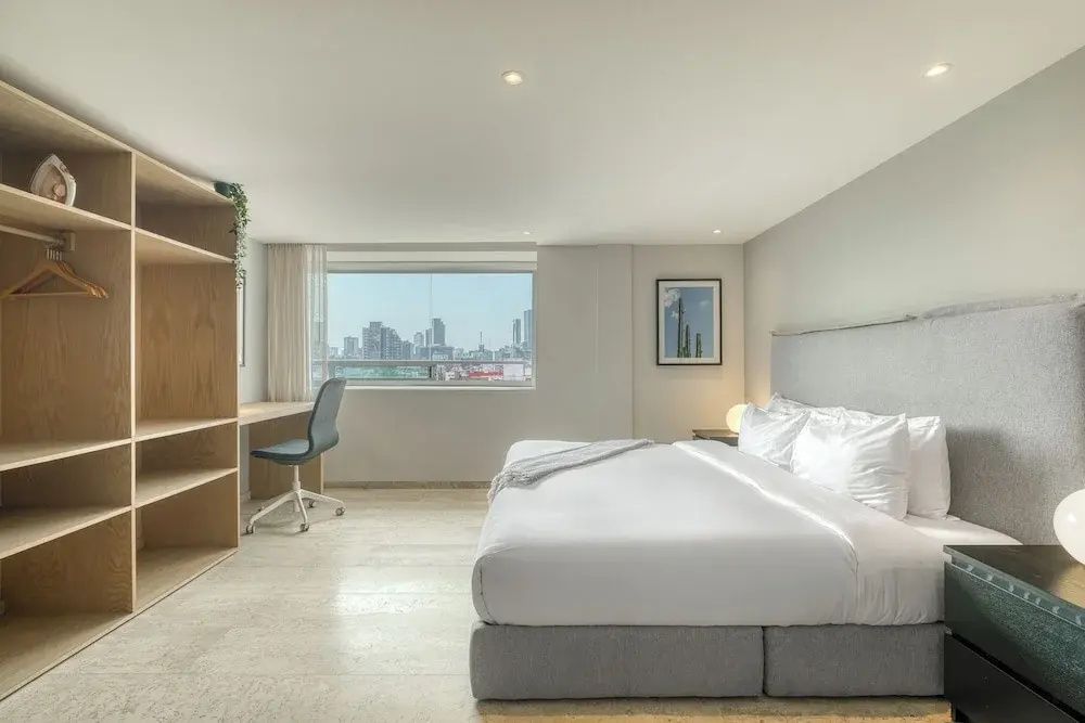 Hell eingerichtetes Hotelzimmer mit Doppelbett, Schreibtisch und Fenster.