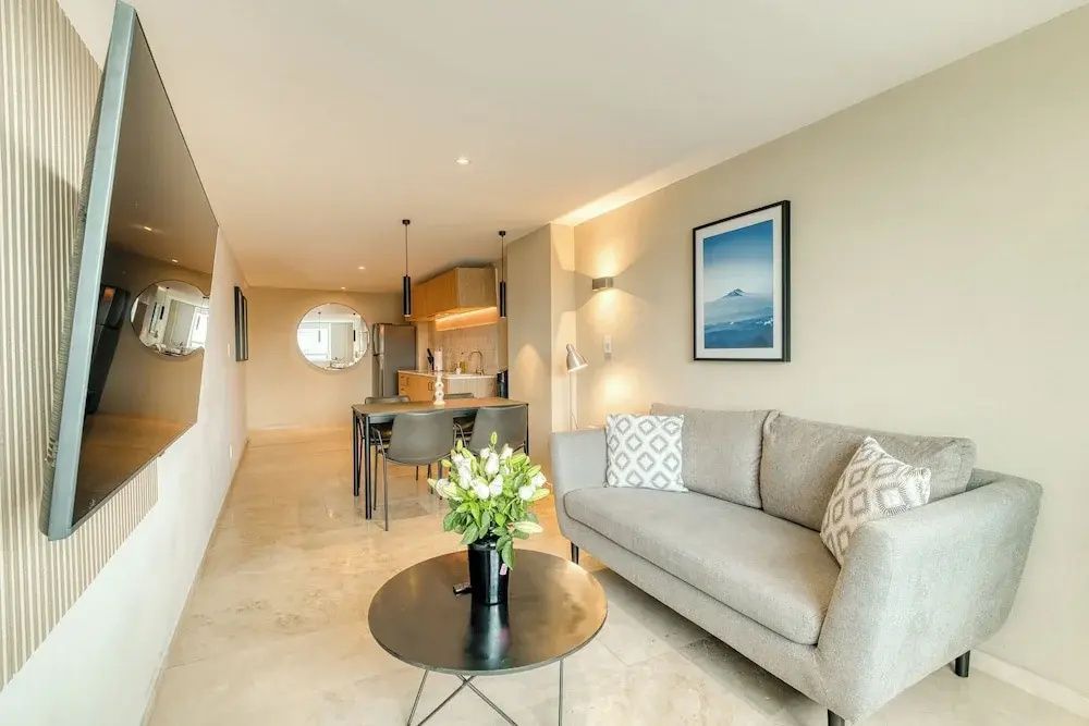 Modernes Wohnzimmer mit grauem Sofa, Couchtisch, Esstisch und offener Küche.