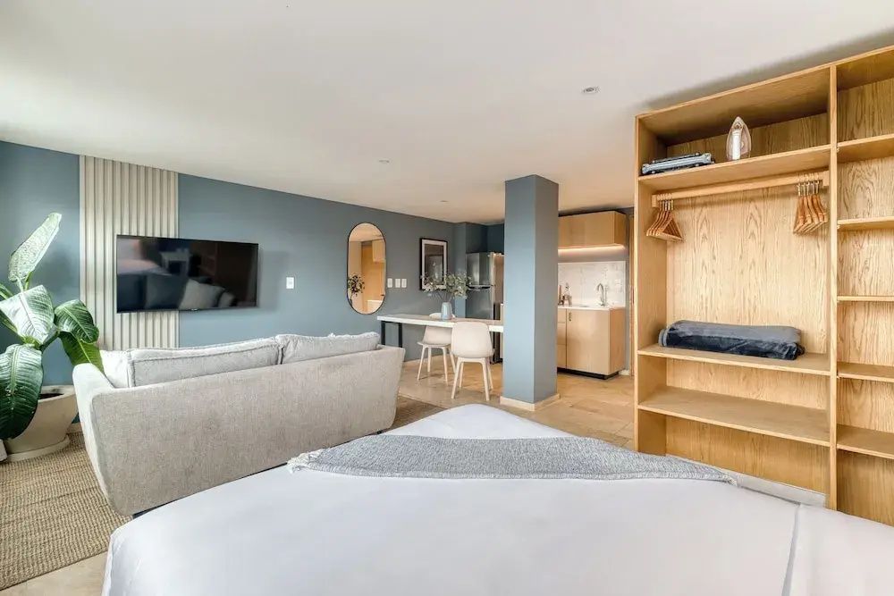 Offener Wohnbereich mit Sofa, Holzregal, Esstheke und hellblauen Wänden.