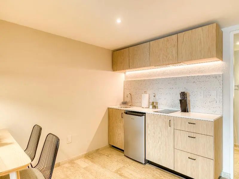 Kompakte Küchenzeile aus hellem Holz mit Kühlschrank, Spüle und Kochfeld.