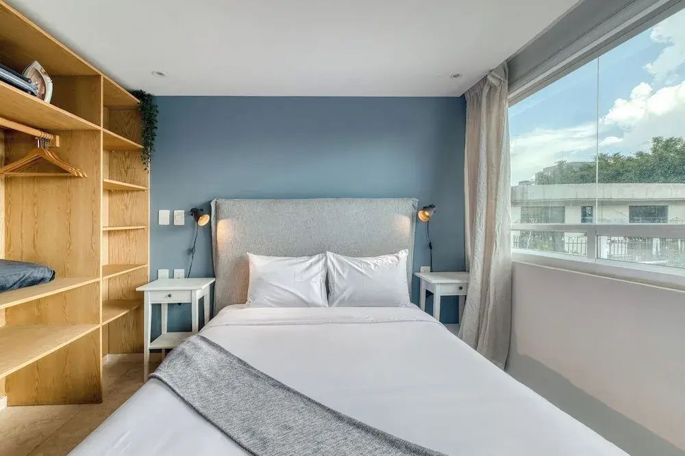 Doppelbett mit hellgrauem Kopfteil, weißen Nachttischen und blau gestrichener Wand.