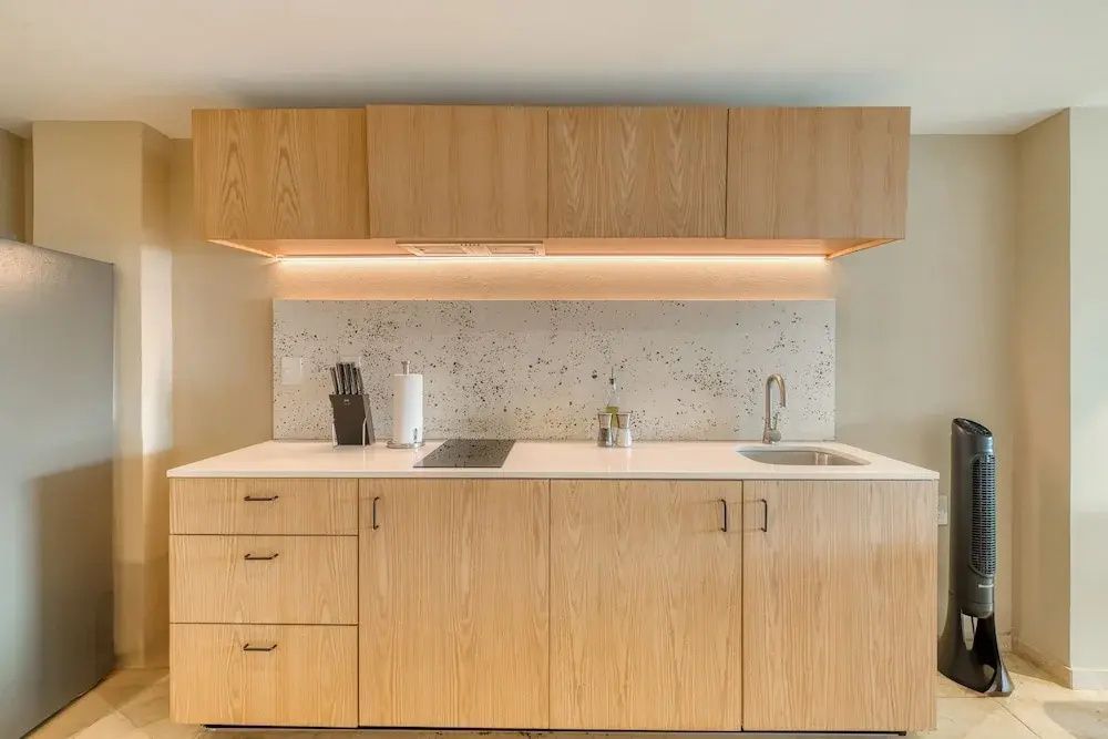Moderne Küchenzeile aus Holz mit Spüle, Kochfeld und beleuchteter Rückwand.