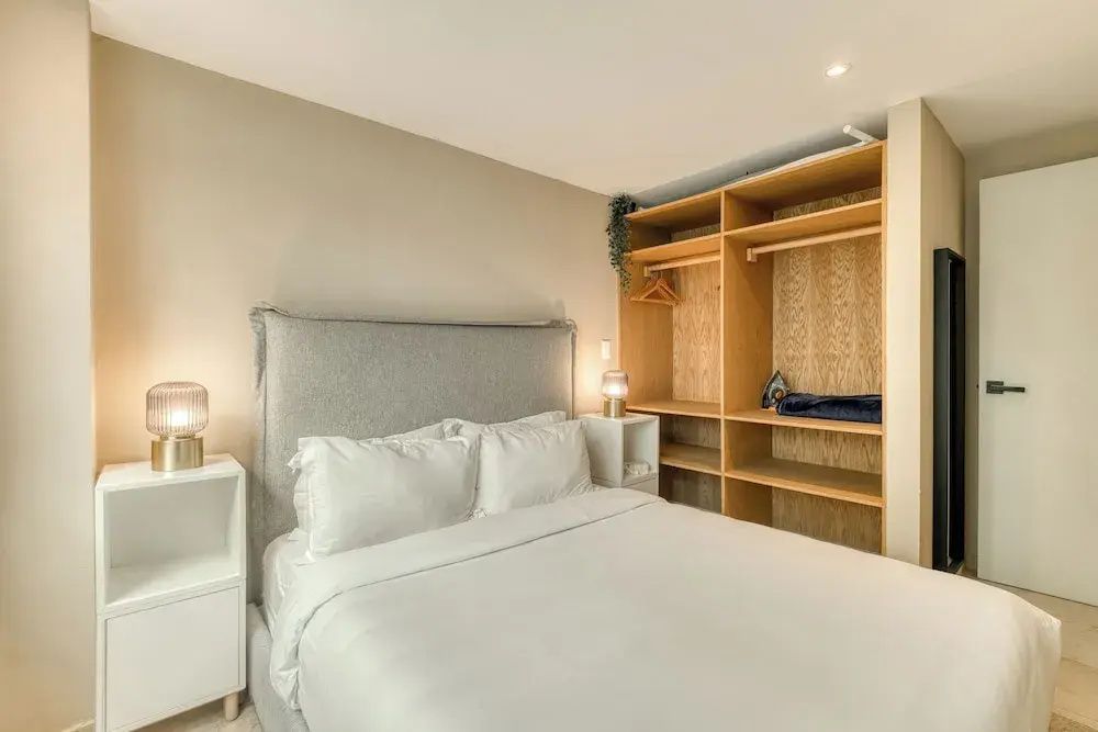 Schlafzimmer mit bezogenem Doppelbett und offenem Kleiderschrank aus Holz.