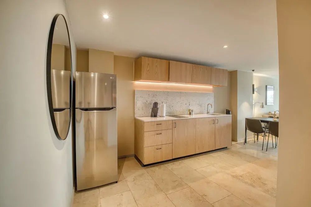 Küche im Apartment mit Edelstahl-Kühlschrank, Holzschränken und hellen Fliesen.