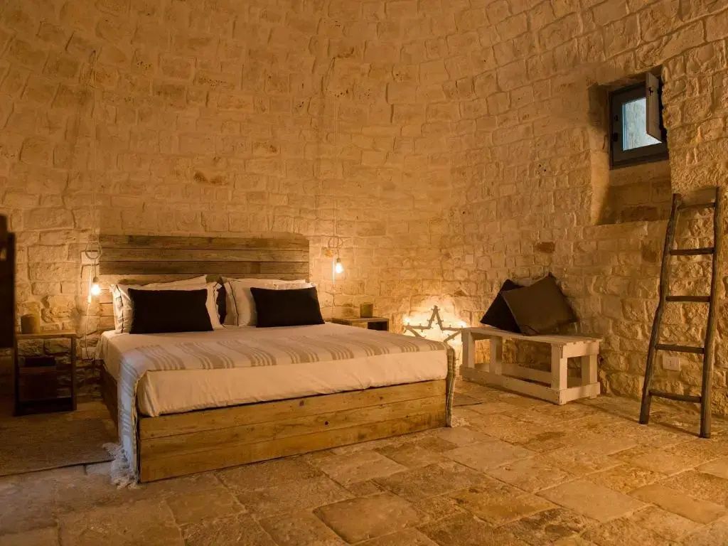 Schlafzimmer in einem Natursteingewölbe mit rustikalem Doppelbett und dekorativer Beleuchtung.