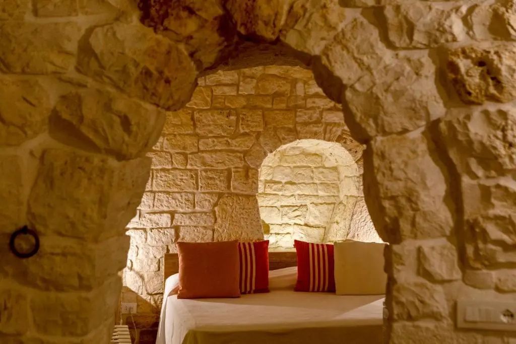 Bett mit bunten Kissen in einer beleuchteten Rundbognische aus Naturstein.