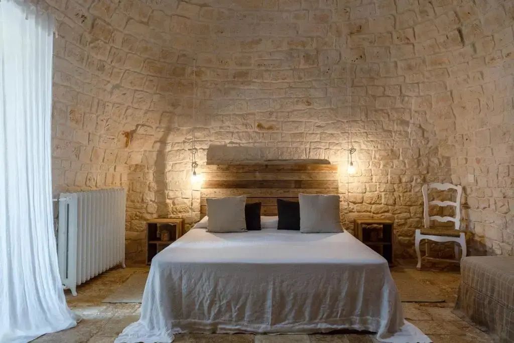 Schlafzimmer unter einer Steinkuppel mit Doppelbett, Kopfteil aus Holz und Nachttischen.