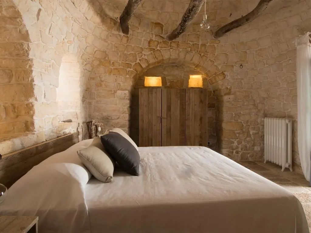 Gefliestes Schlafzimmer mit Holzschrank, Doppelbett und historischem Steingewölbe.