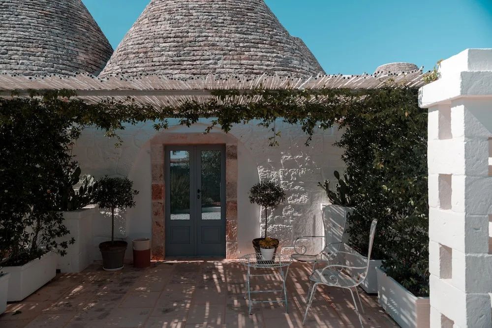 Eine gepflasterte Terrasse mit Stühlen und Tischen vor einem weiß getünchten Trullo.