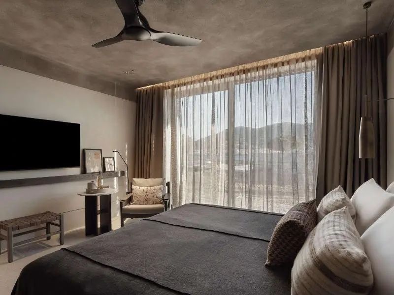 Helles Hotelzimmer mit Doppelbett, Sessel und großer Fensterfront.