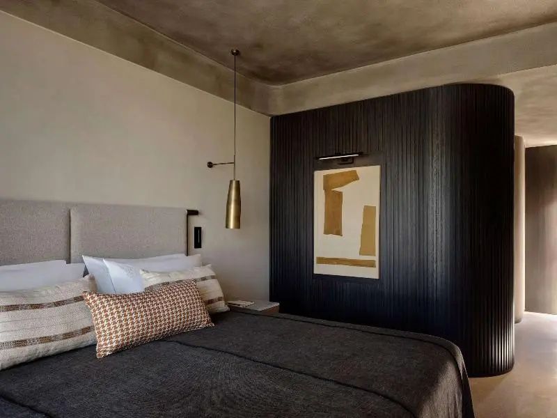 Doppelbett mit dunkler Tagesdecke, Holzverkleidung an der Wand und hängender Lampe.