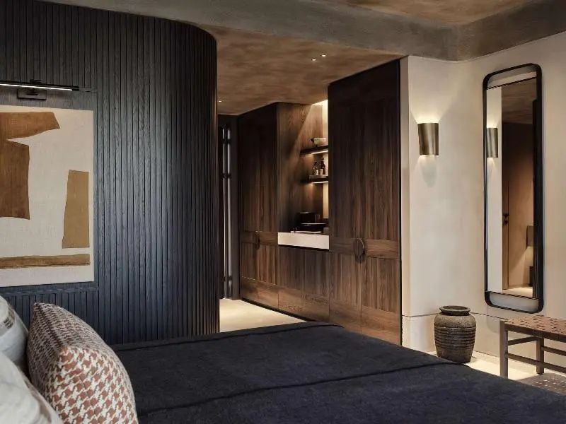 Hotelzimmer mit dunkler Holzverkleidung, integriertem Schrankbereich und Bett im Vordergrund.