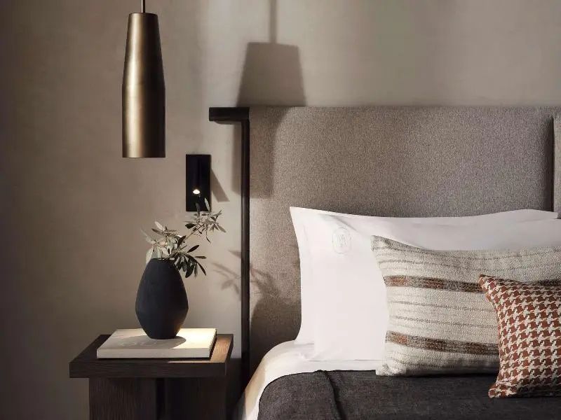 Nachttisch mit einer kleinen Vase und einer Lampe neben dem gepolsterten Kopfteil des Bettes.