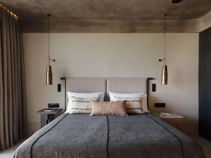 Doppelbett mit grauer Tagesdecke und zwei hängenden Messinglampen an der Wand.