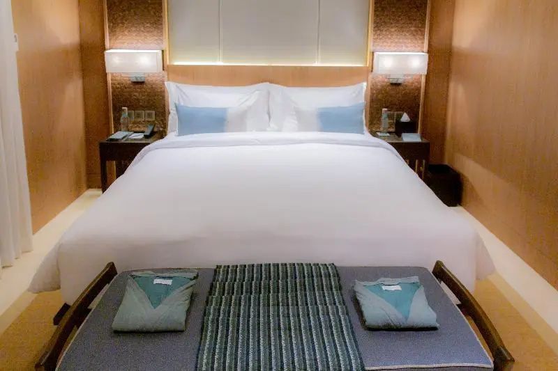 Großes Doppelbett mit weißer Bettwäsche und Bettbank mit zusammengelegten Mänteln.