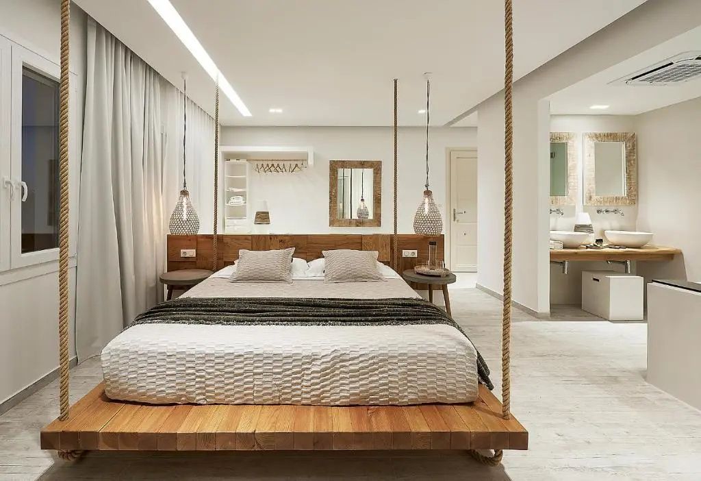 Doppelbett aus Holz mit Seilaufhängung, Nachttischlampen und Blick in das Badezimmer.