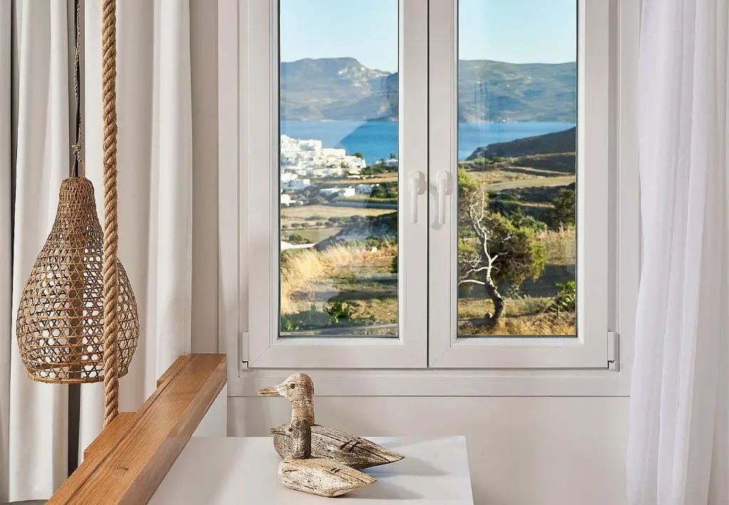 Fenster mit Ausblick auf eine Küstenlandschaft, das Meer und weiße Häuser eines Dorfes