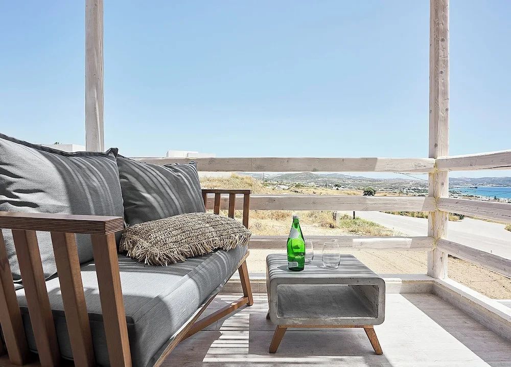 Balkon mit Sitzmöbeln aus Holz und grauen Kissen sowie Blick auf Hügel und den blauen Himmel.