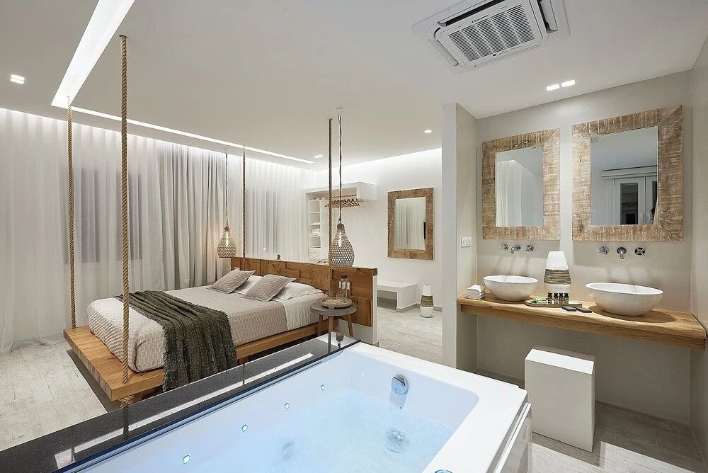 Offene Hotelsuite mit eingebautem Whirlpool im Vordergrund und einem Doppelbett dahinter.