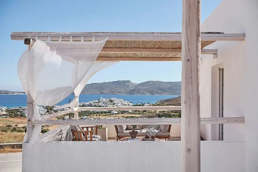 Blick von der Terrasse über eine weiße Küstenstadt auf das Meer und gegenüberliegende Berge.