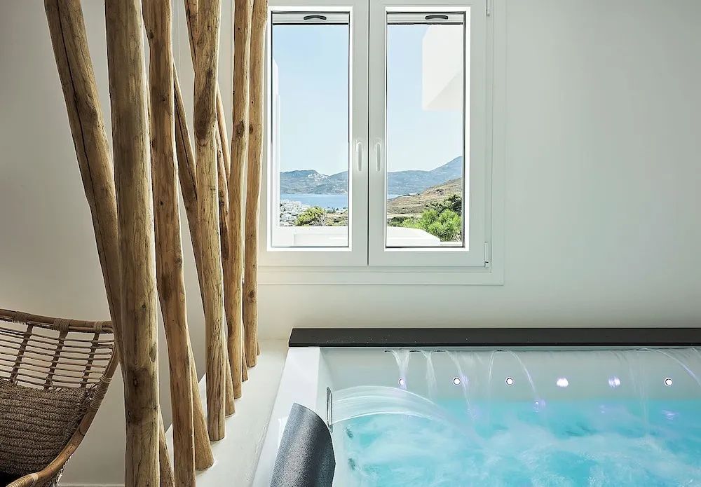 Whirlpool mit sprudelndem Wasser vor einem Fenster mit Blick auf das Meer und Hügel.