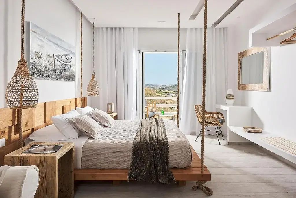 Helles Schlafzimmer mit an Seilen aufgehängtem Holzbett und Blick ins Freie.