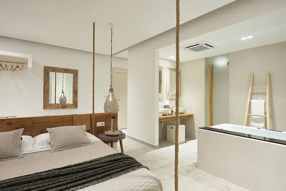 Geräumige Suite mit hellem Fliesenboden, Hängeseilen am Bett und offener Badewanne.