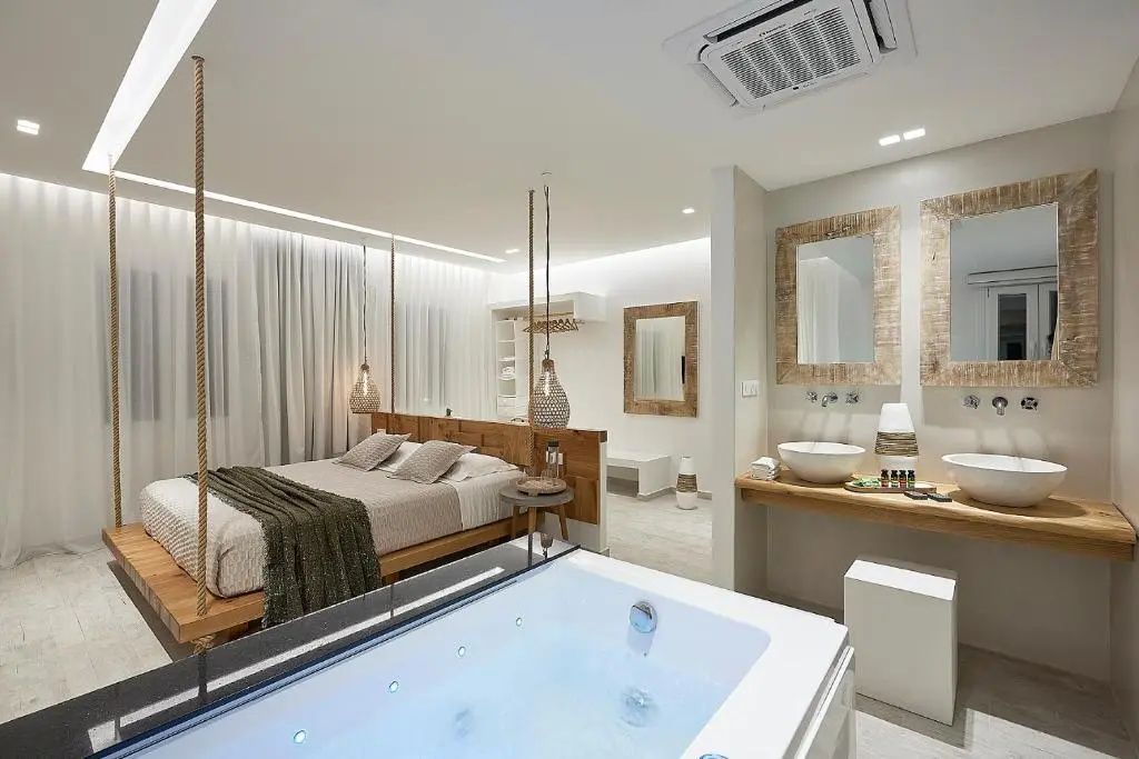 Offene Suite mit einem Whirlpool im Raum, Doppelbett und Waschtisch im Hintergrund.