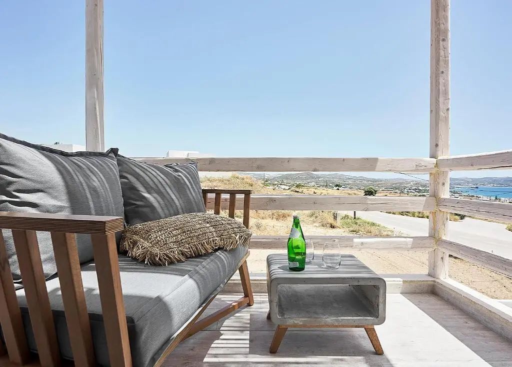 Eine überdachte Terrasse mit Holzsofa und Couchtisch bietet Ausblick auf die hügelige Landschaft.