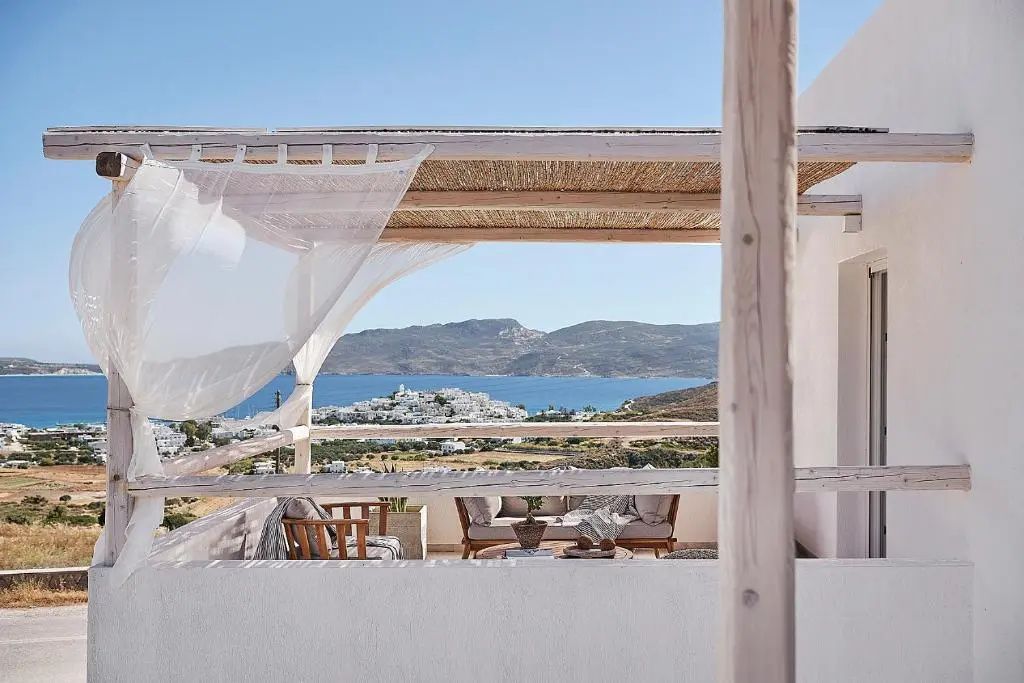 Überdachte Terrasse mit Holzmöbeln und Blick auf das Meer sowie ein Küstendorf.