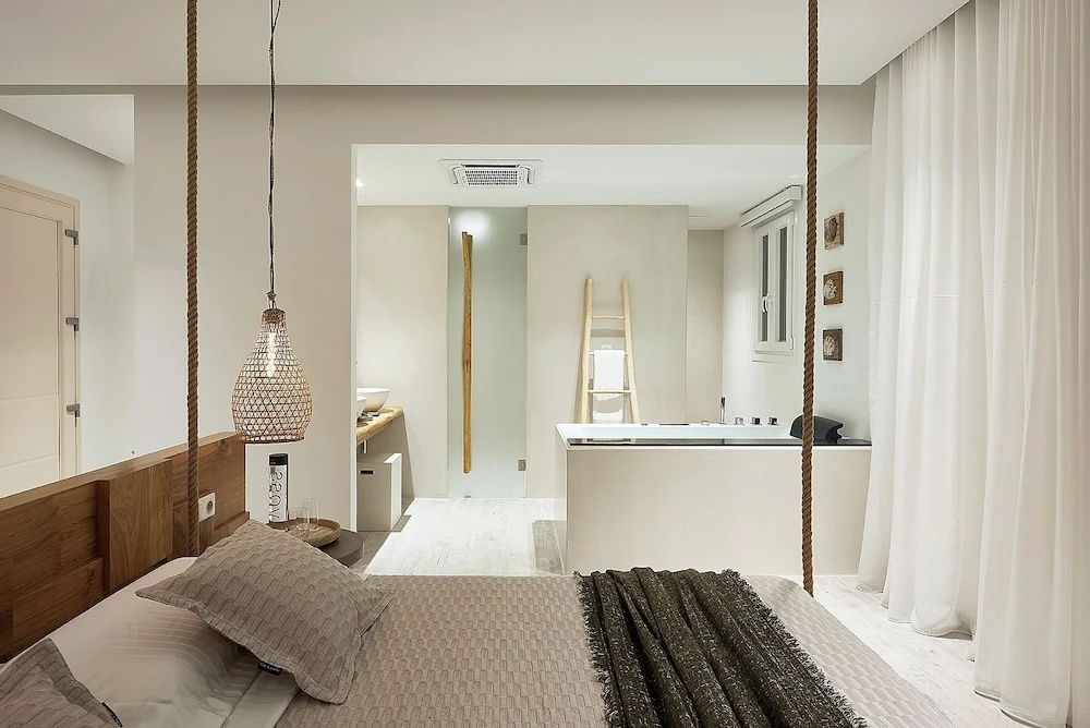 Helles Hotelzimmer mit Bett im Vordergrund und angrenzendem Badezimmerbereich mit Whirlpool.