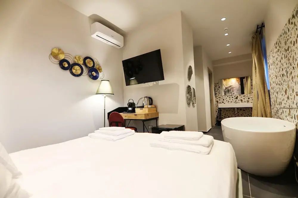 Modern eingerichtetes Zimmer mit Doppelbett, Fernseher, Schreibtisch und Badewanne.