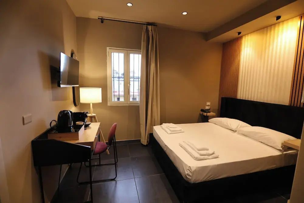 Hell eingerichtetes Hotelzimmer mit großem Doppelbett, Schreibtisch und TV an der Wand.