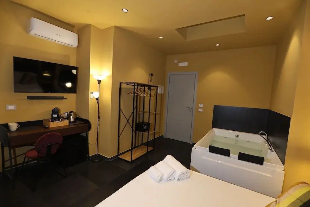 Blick in das Hotelzimmer mit offenem Kleidergestell, Schreibtisch und Whirlpool.