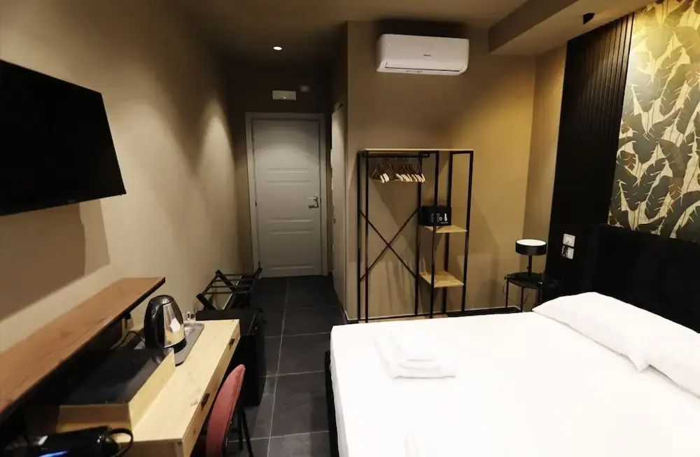 Zimmerbereich mit Bett, Holzschreibtisch, offenem Kleiderständer und Eingangstür.