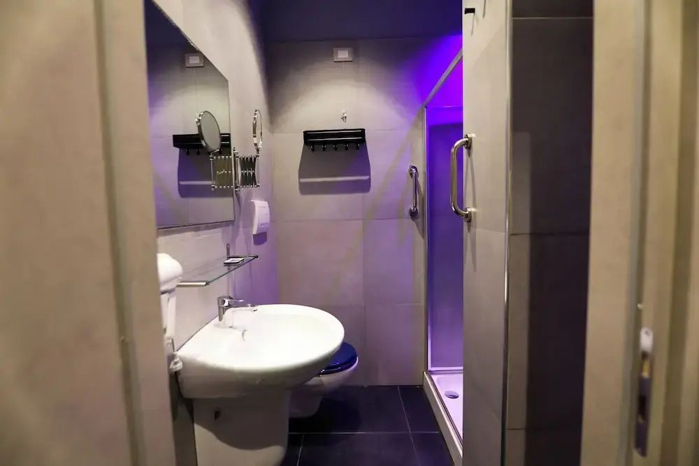Badezimmer mit Waschtisch, Spiegel, WC und einer Dusche mit farbiger Beleuchtung.