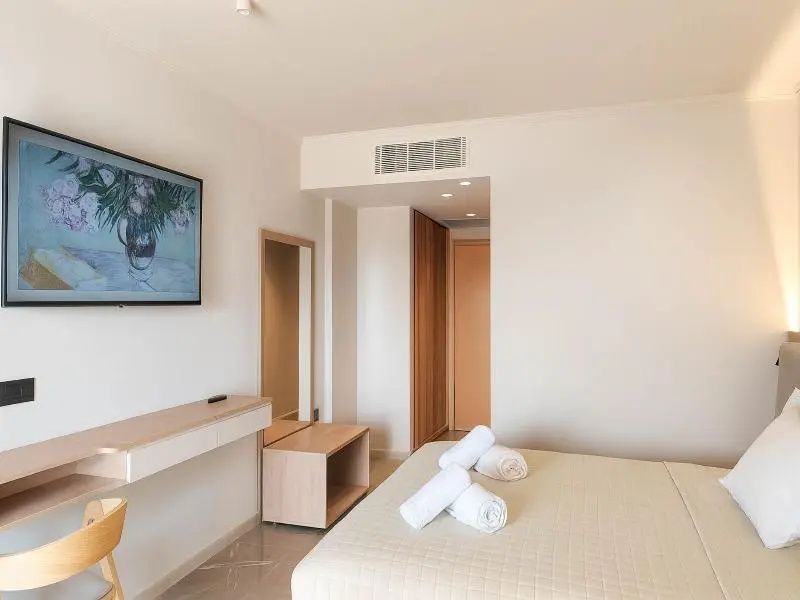 Helles Hotelzimmer mit Doppelbett, zusammengerollten Handtüchern, Schreibtisch und Wandfernseher.
