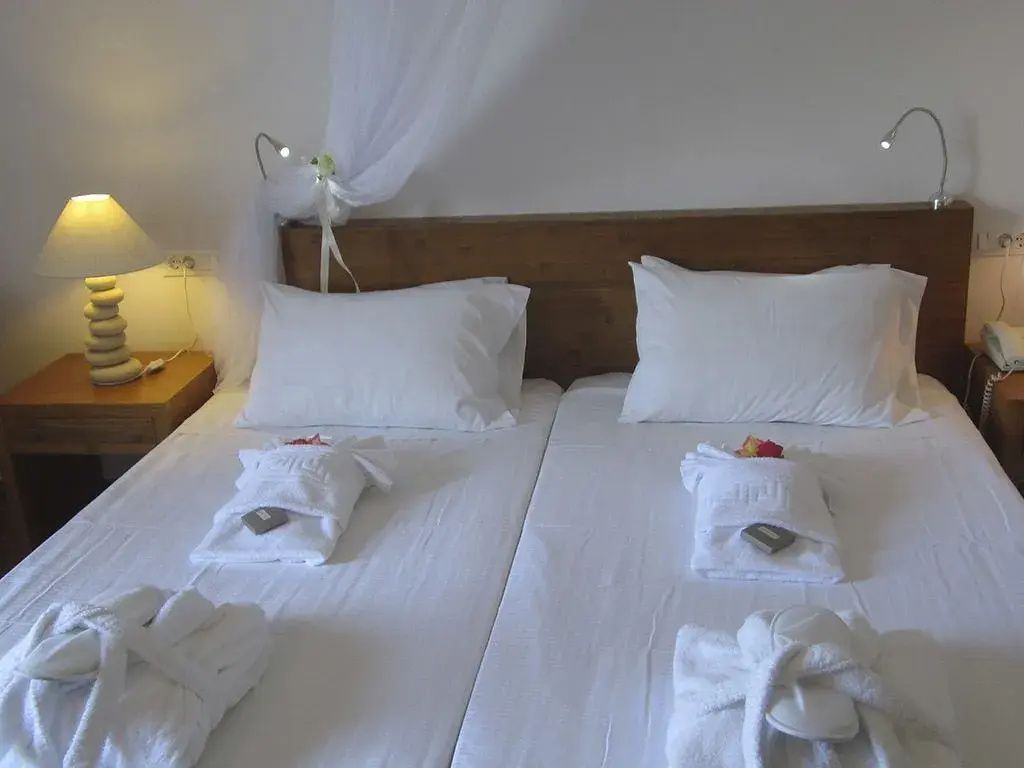 Doppelbett mit weißer Bettwäsche, Holzkopfteil, Moskitonetz und bereitgelegten Bademänteln.