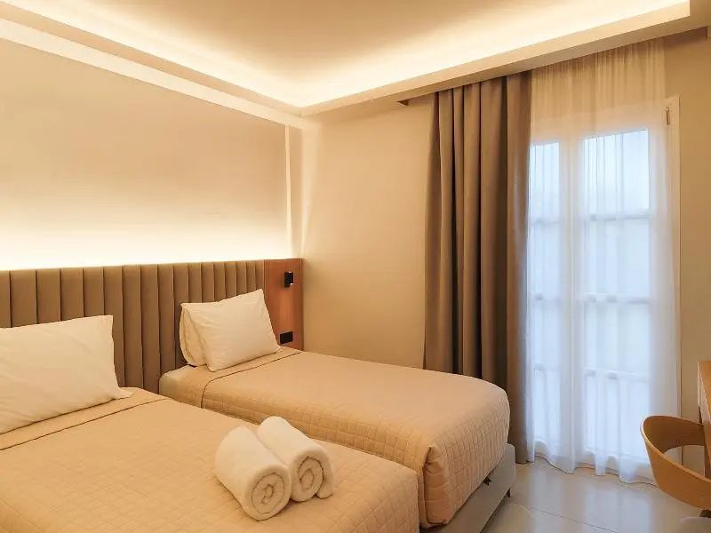 Schlafzimmer mit zwei Einzelbetten, weißer Bettwäsche, indirekter Beleuchtung und hellen Vorhängen.