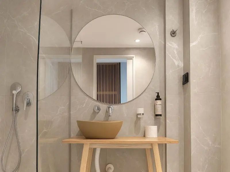 Moderner Waschtisch mit ovalem Waschbecken, rundem Wandspiegel und Seifenspender im Badezimmer.